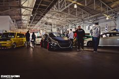 several cars are parked in a garage with people standing around them and talking to each other