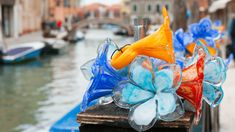 colorful glass flowers are sitting on a wooden post in front of a canal with gondola boats