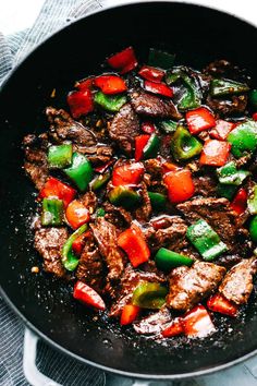 beef and peppers cooking in a skillet on top of a stovetop with a towel