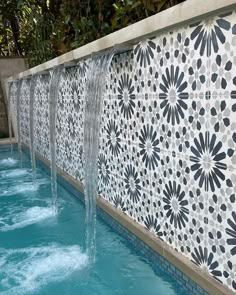 an outdoor pool with water running from the side and decorative tiles on the back wall