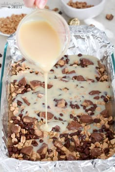 someone pouring milk on top of a dessert in a baking pan with chocolate chips and almonds