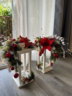 two christmas wreaths on stands in front of a window with white drapes and red poinsettis