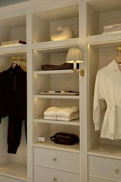 an open closet with white shelves and clothes on it's sides, along with other items