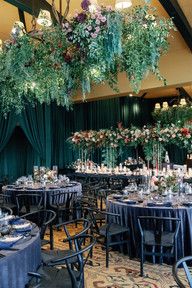 the tables are set up with blue linens and floral centerpieces hanging from the ceiling