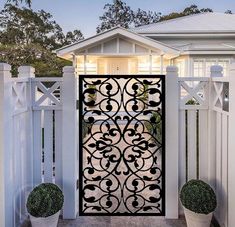 a white house with an iron gate and two potted plants on the front porch