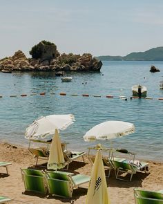 several lawn chairs and umbrellas are on the sand near the water's edge