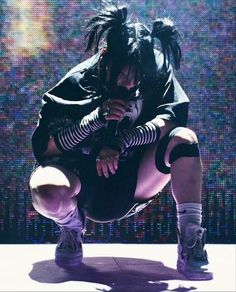 a woman in black and white outfit crouching on the ground with her legs crossed