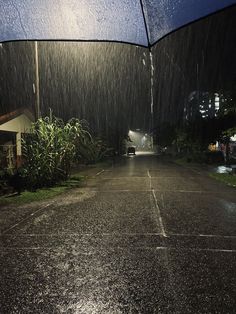 an open umbrella sitting on the side of a wet road at night with rain coming down