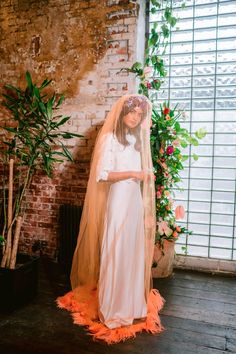 a woman wearing a veil and dress standing in front of a brick wall with flowers