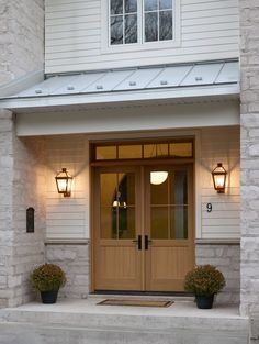 two potted plants are sitting in front of the entrance to a white house with wood doors and windows