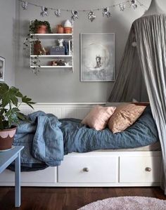 a bed with blue sheets and pillows on top of it next to a shelf filled with potted plants