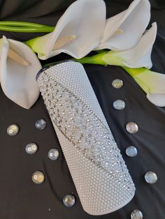 a white vase sitting on top of a black table next to flowers and pearls,