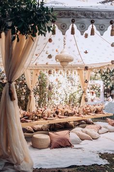 an outdoor wedding setup with lots of pillows and flowers on the ground, hanging from ceiling