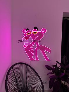 a pink neon sign that is on the wall next to a chair and a fan