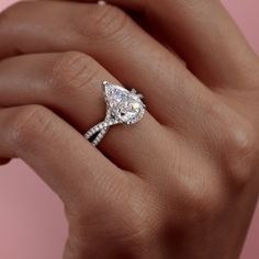 a woman's hand holding an engagement ring with a pear shaped diamond on it