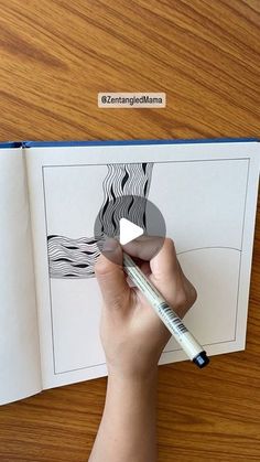 a person is holding a pencil and drawing an image in a book on a wooden table