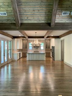 an empty kitchen and living room with wood flooring in the center, large open space between two ceiling beams