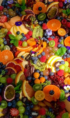 an assortment of fresh fruit is displayed on a plate with green leaves and oranges