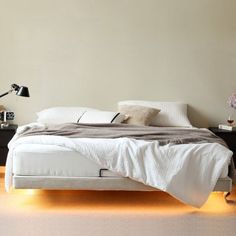 a white bed sitting on top of a wooden floor next to a night stand and lamp