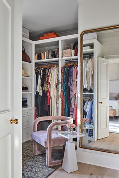 the closet is full of clothes, shoes and handbags on hangers in front of a large mirror