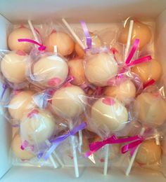 a box filled with cake pops covered in white frosting and pink ribbon tied around them