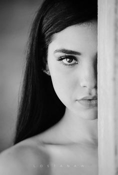 a black and white photo of a woman's face peeking out from behind a wall