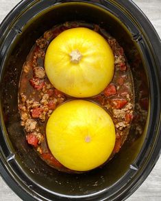 two yellow tomatoes are in the crock pot with meat and vegetables inside it, ready to be cooked