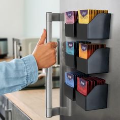 a person's hand is pointing at a wall mounted coffee cup holder on the side of a kitchen counter