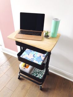 a laptop computer sitting on top of a wooden table next to a cup and plant