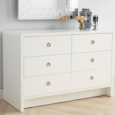 a white dresser with two vases on top of it next to a large mirror