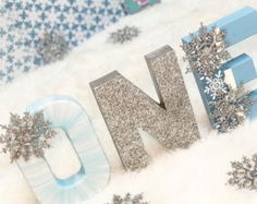 the word snow spelled out in silver glitter and surrounded by snowflakes on a white background