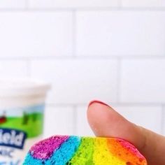 a hand holding a half eaten rainbow cake next to a cup of yogurt