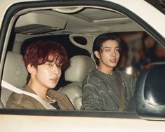 two young men sitting in the back seat of a car, one with red hair