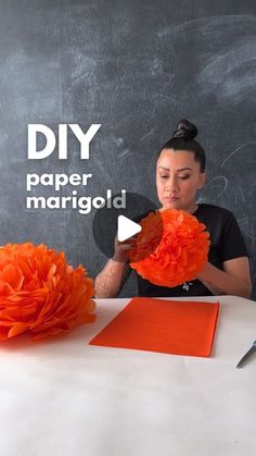 a woman sitting at a table with orange flowers in front of her and the words diy paper marrigld