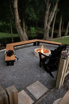 an outdoor fire pit with two chairs and a table in the middle surrounded by trees