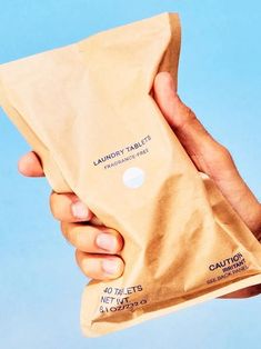 a hand holding a brown paper bag with the label laundry sheets on it, against a blue background