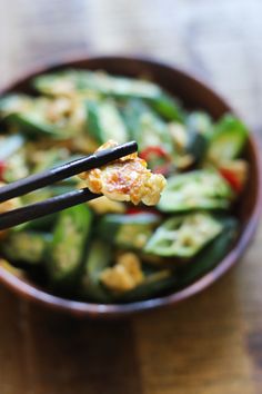 two chopsticks are holding up some food in a bowl on a wooden table