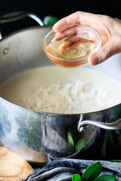 someone is adding olive oil to rice in a pot on the stove top with green leaves