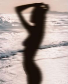 a blurry image of a woman standing on the beach with her arms behind her head