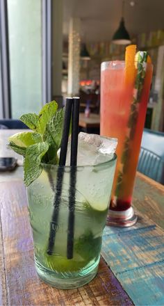 two glasses filled with drinks sitting on top of a wooden table next to each other