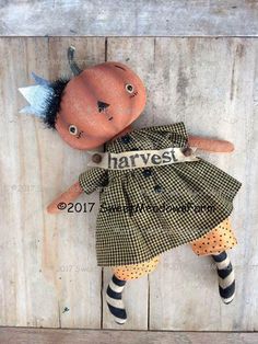 an orange doll with black hair wearing a green dress and striped socks is hanging on a wooden wall