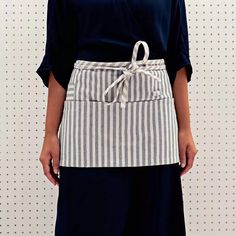 a woman wearing an apron with white and black stripes on the front, standing in front of a wall