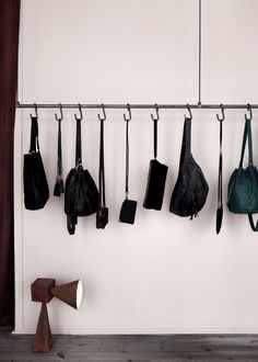 several purses hanging from hooks on a white wall next to a wooden bench and coat rack