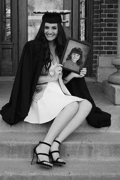 a woman sitting on the steps with her graduation cap and gown over her head, holding a framed photo