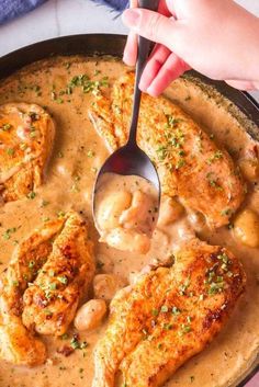 someone is spooning some chicken with gravy in a skillet on the table