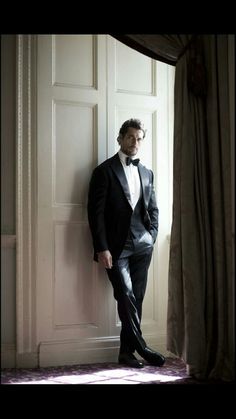 a man in a tuxedo leaning against a wall