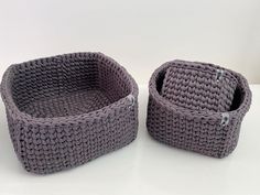 two gray knitted baskets sitting on top of a white table next to each other