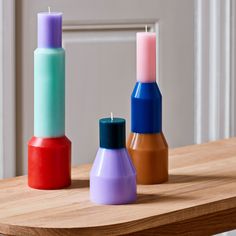 three different colored candles sitting on top of a wooden table next to eachother