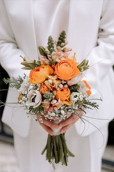 a person in a white suit holding a bouquet of orange and white flowers on their left hand