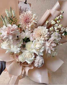 a bouquet of white and pink flowers in a vase next to a brown ribbon on a wall